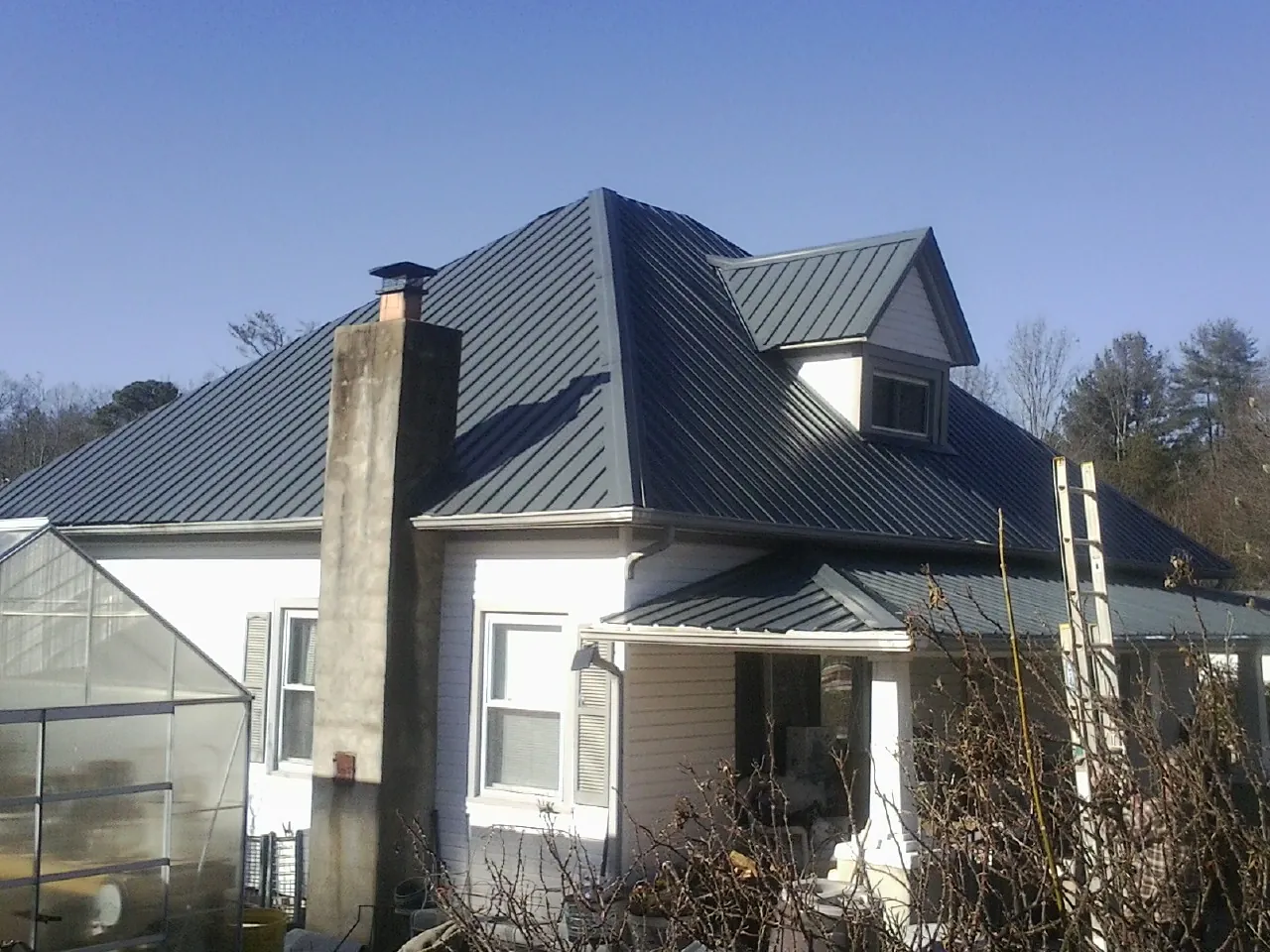 Dark blue standing seam metal roof on a white farmhouse with dormer in Winthrop Harbor