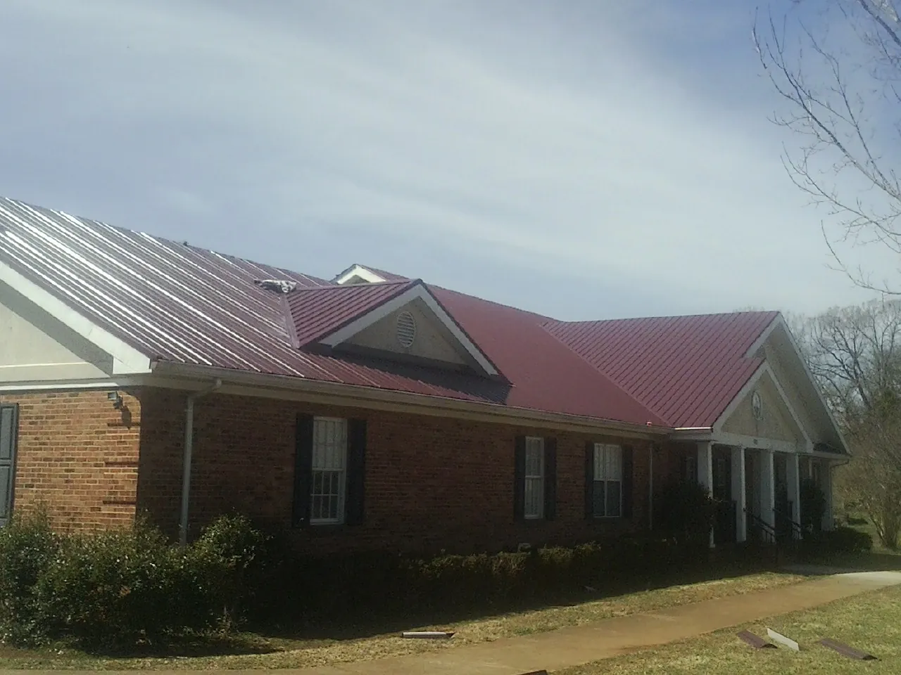 Red metal roof with gabled entries on a long brick building, from a Hail Damage Roof Repair job in Winthrop Harbor