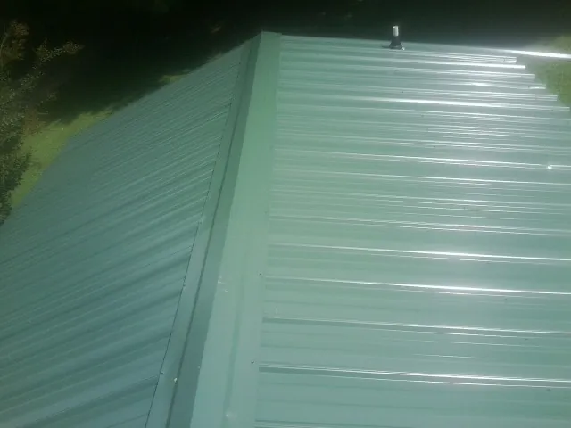 New green metal panels meeting at the ridge of a roof — Flat Roof Repair work by our crew in Winthrop Harbor