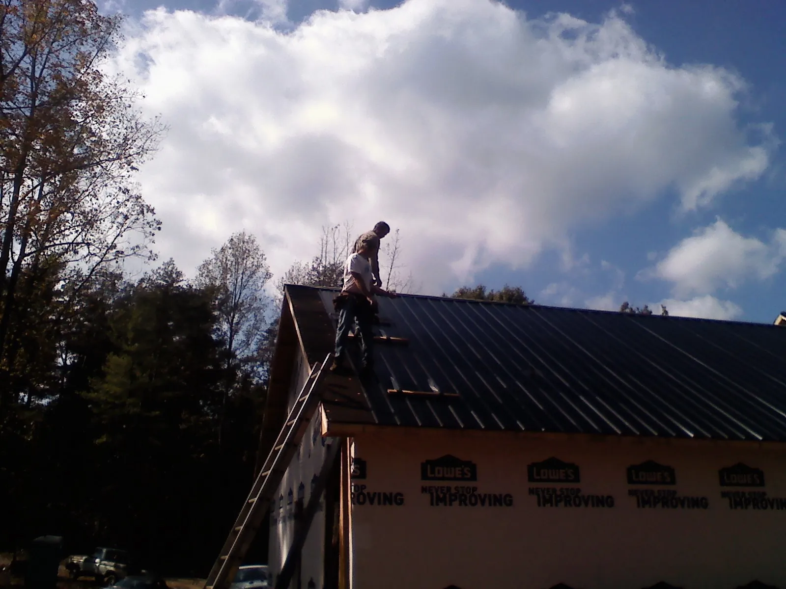Roofer fastening dark metal panels high against a cloudy sky, from a Roof Inspection job in Winthrop Harbor