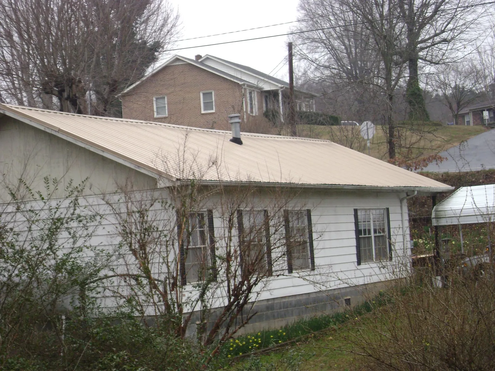 Tan metal roof on a white sided house set into a hillside — Commercial Roofing by Roofing Brothers in Winthrop Harbor